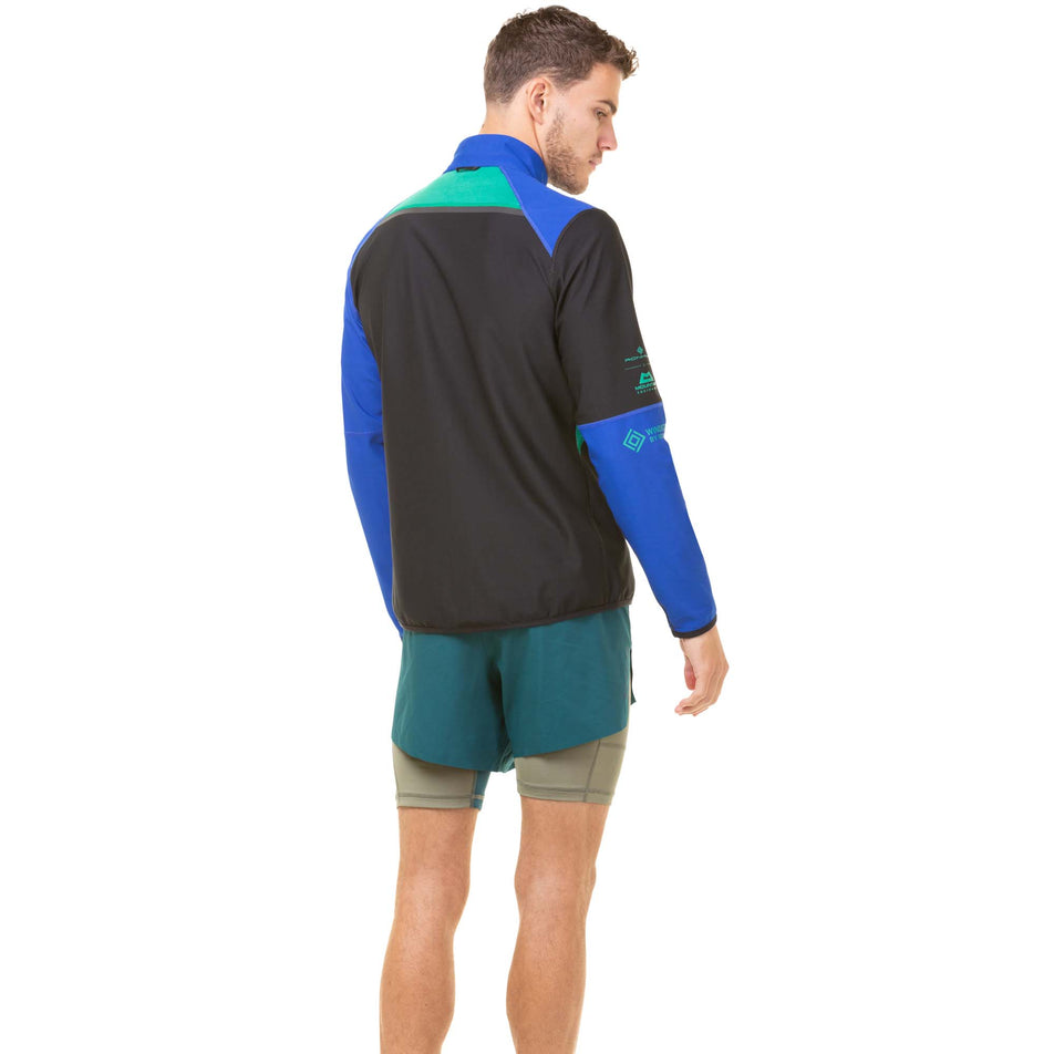 Back view of a model wearing a Ronhill Men's Tech Gore-Tex Windstopper Jacket in the Black/Cobalt colourway. Model also wearing a pair of green Ronhill shorts. (8032213565602)