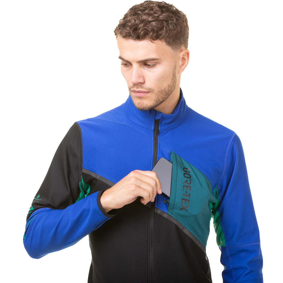 Front view of a model demonstrating that a phone can be stored in the chest pocket of a Ronhill Men's Tech Gore-Tex Windstopper Running Jacket in the Black/Cobalt colourway (8032213565602)