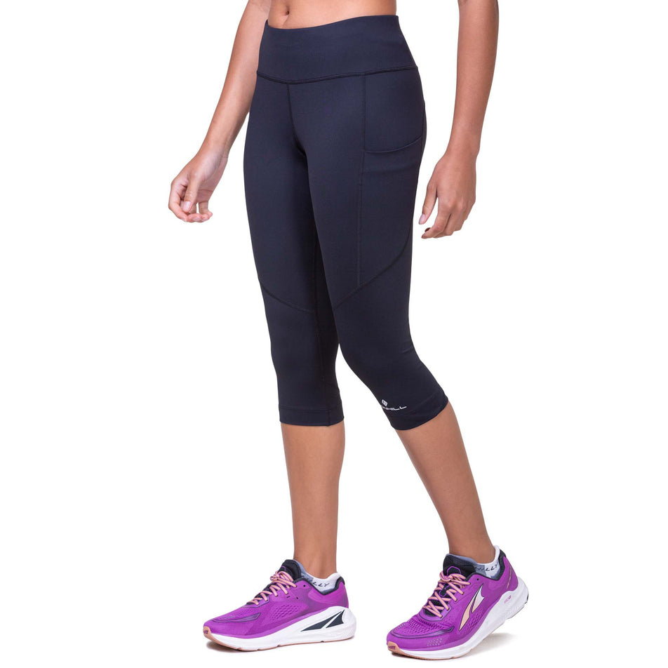 Front view of a model wearing the Ronhill Women's Tech Capri in the Black/Bright White colourway. Model is also wearing Altra running shoes. (8160832422050)