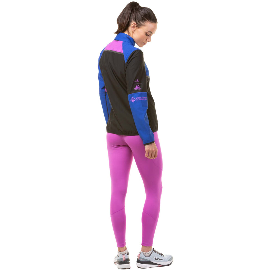 Back view of a model wearing a Ronhill Women's Tech Gore-Tex Windstopper Jacket in the Black/Cobalt colourway. Model is also wearing a Ronhill running leggings and Altra running shoes. (8024339841186)