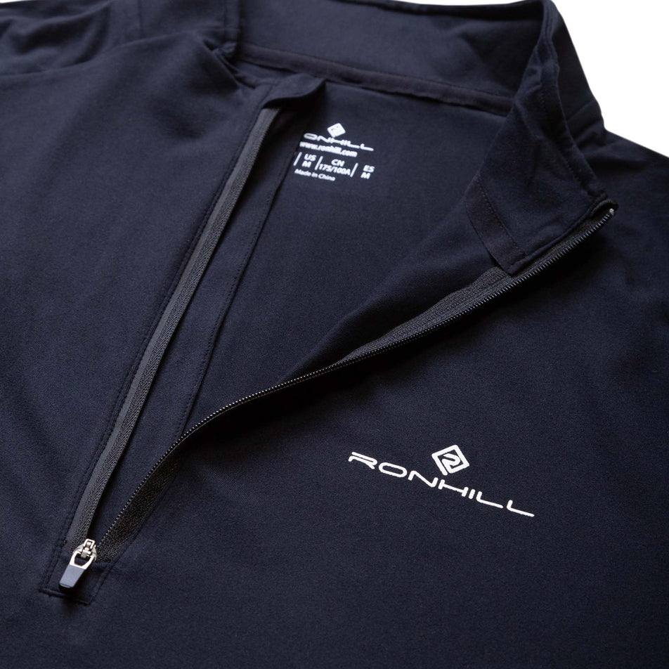 Close-up view of the front zip and Ronhill logo on a Ronhill Men's Core Thermal 1/2 Zip in the Black/Bright White colourway. (8032268517538)