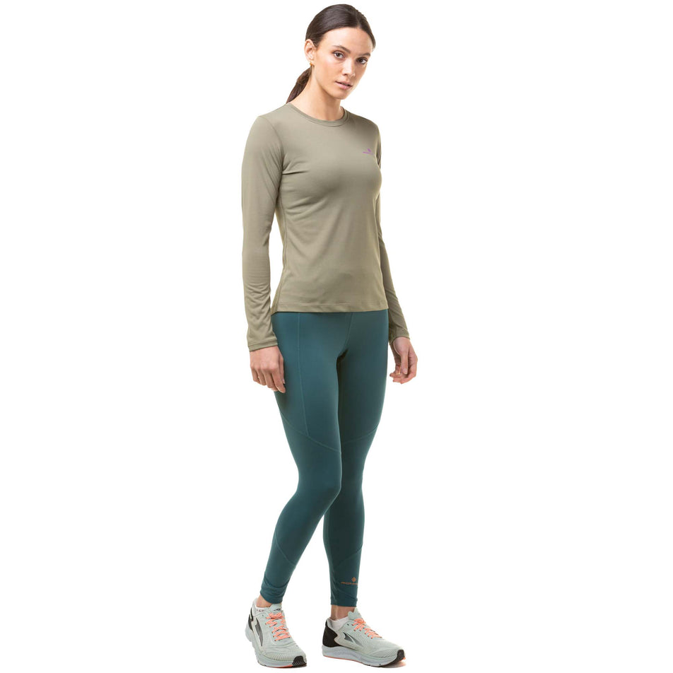 Front view of a model wearing a pair of Ronhill Women's Tech Tights in the Deep Lagoon/Copper colourway. Model also wearing a green Ronhill long sleeve top and grey Altra running shoes. (8024370315426)