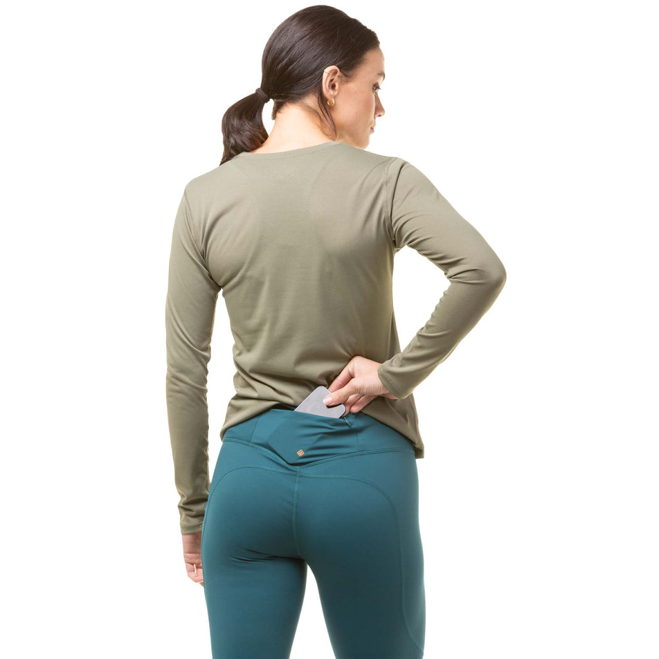 Back view of a model demonstrating that a phone can be stored in the zipped back pocket on a pair of Ronhill Women's Tech Tights in the Deep Lagoon/Copper colourway. Model also wearing a green Ronhill long sleeve top. (8024370315426)
