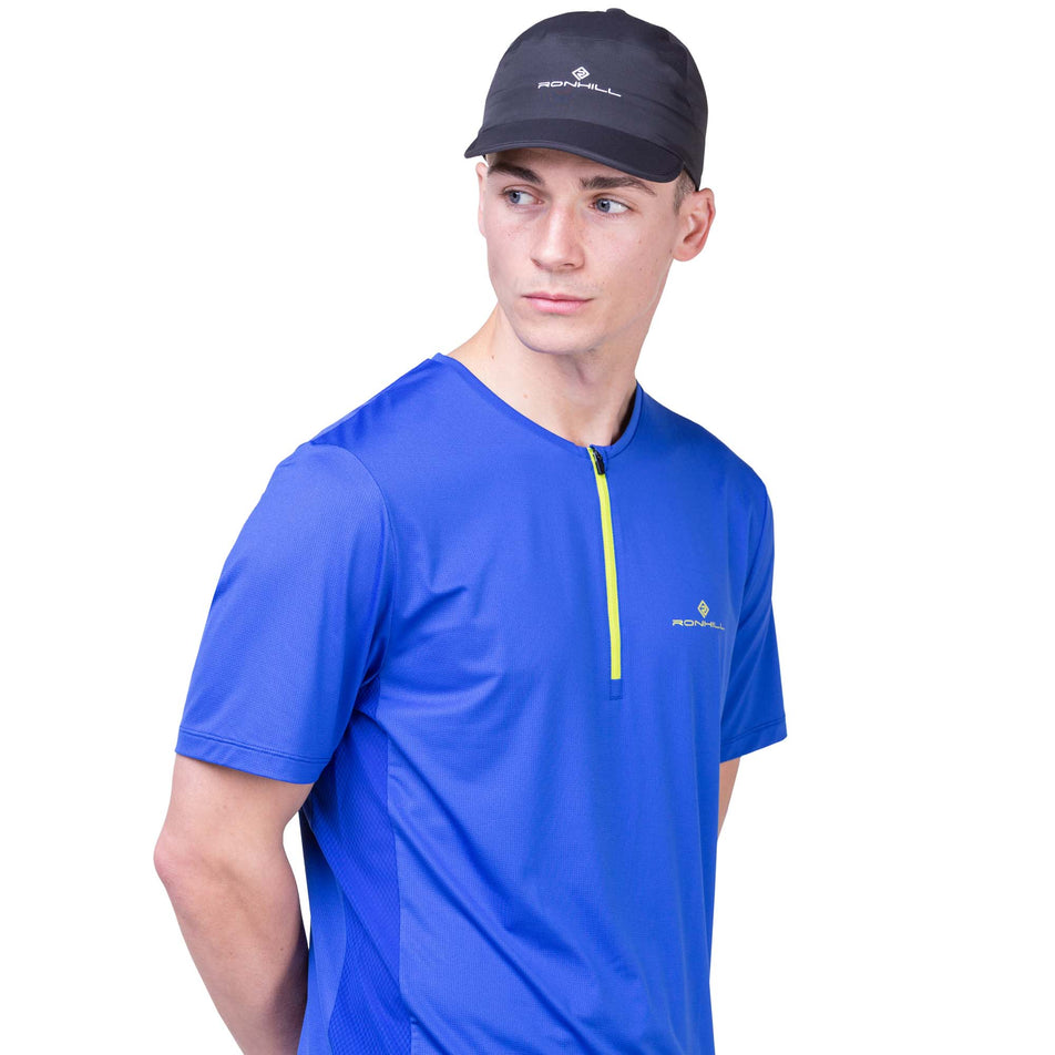Front view of a model wearing a Ronhill Unisex Sunlight Cap in the All Black colourway. Model is also wearing a Ronhill running top.  (8160951238818)