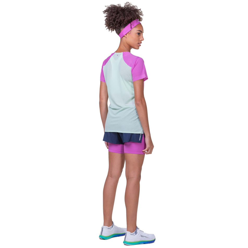 Angled-back view of a model wearing a Ronhill Women's Tech Race S/S Tee in the Fuchsia/Honeydew colourway. Model is also wearing Ronhill shorts and Altra running shoes. (8158803427490)