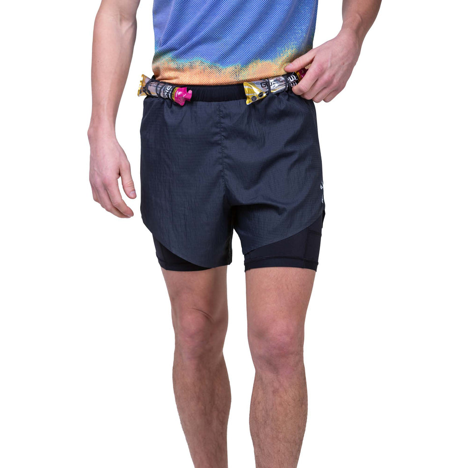 Front view of a model wearing the Ronhill Men's Tech Race Twin Short in the All Black colourway. Model is demonstrating that energy gels can be stored in the elasticated front loops. Model also wearing a Ronhill running top. (8159263883426)