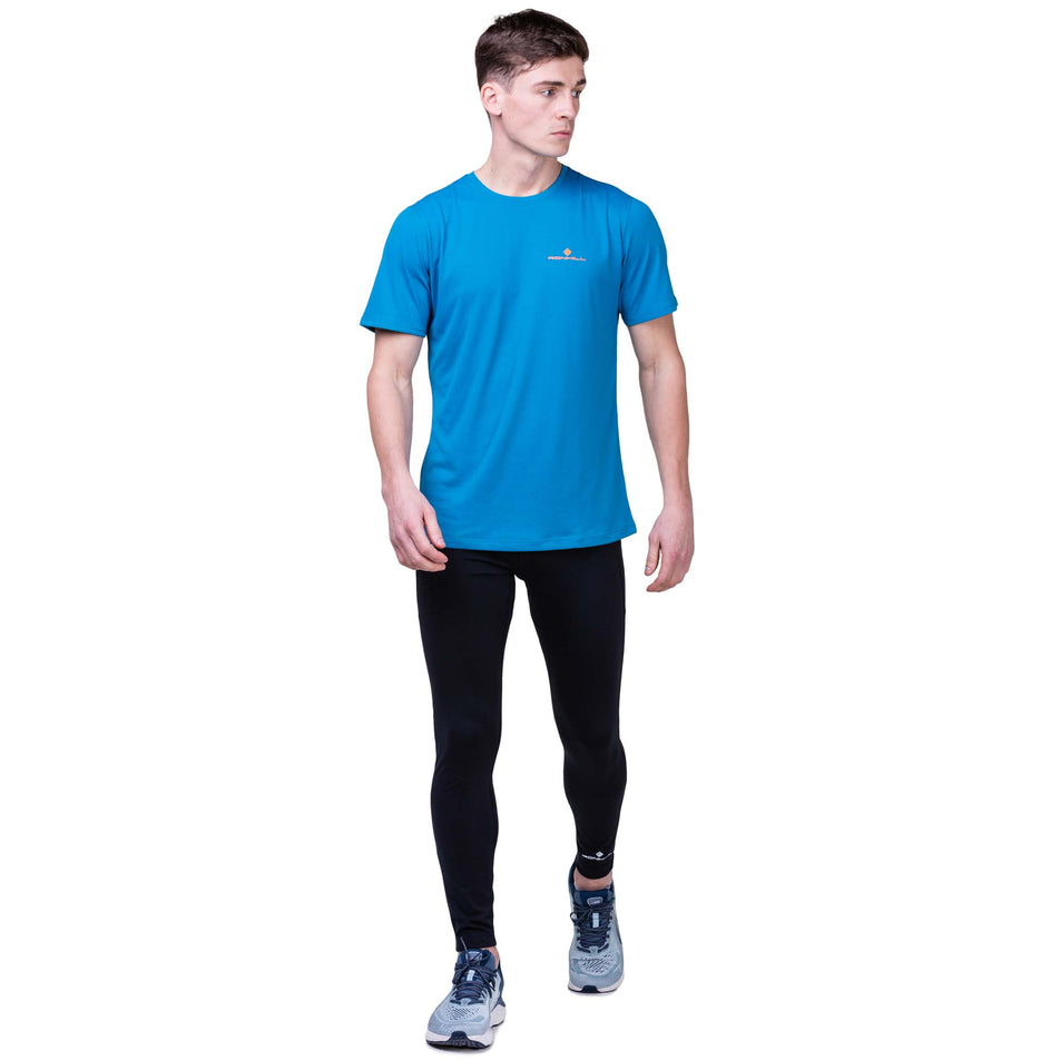 Front view of a model wearing a Ronhill Men's Core S/S Tee in the Petrol/Fluo Orange colourway. Model is also wearing Ronhill tights and Altra running shoes. (8159272698018)