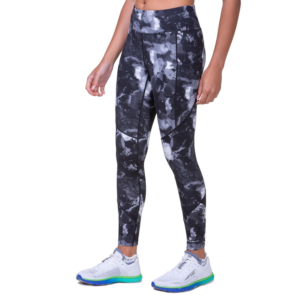 Front view of a model wearing the Ronhill Women's Tech Tight in the Black Ink Drop Media colourway. Model is also wearing Altra running shoes.  (8160850018466)