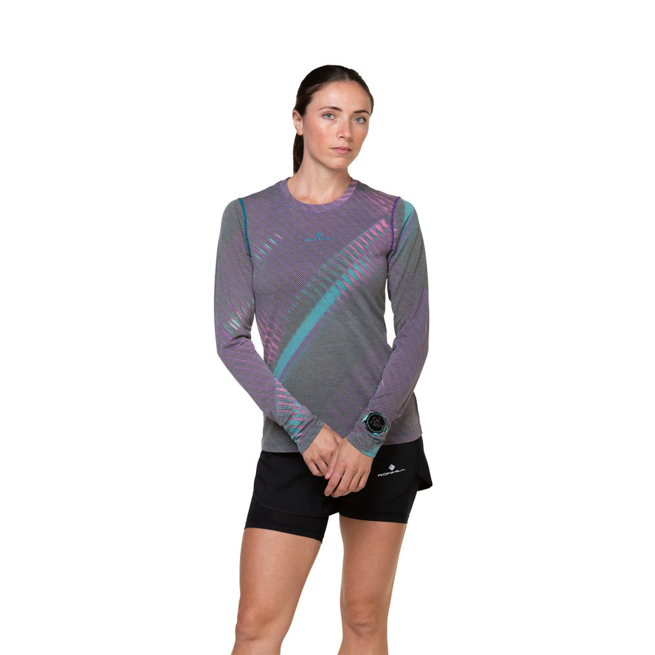 Front view of a model wearing the Ronhill Women's Tech Golden Hour L/S Tee in the Multi Light Reflection colourway. Model is also wearing shorts. (8490067361954)