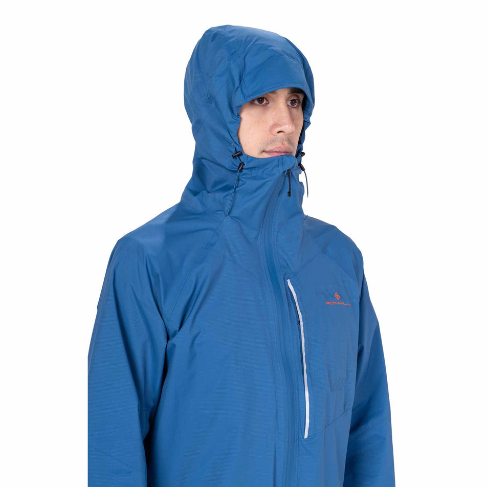 Front view of a model wearing the Ronhill Men's Tech Storm Jacket in the Glacier/Ronhill Red colourway.