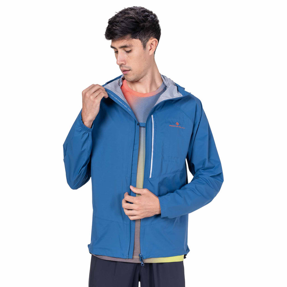 Front view of a model wearing the Ronhill Men's Tech Storm Jacket in the Glacier/Ronhill Red colourway.