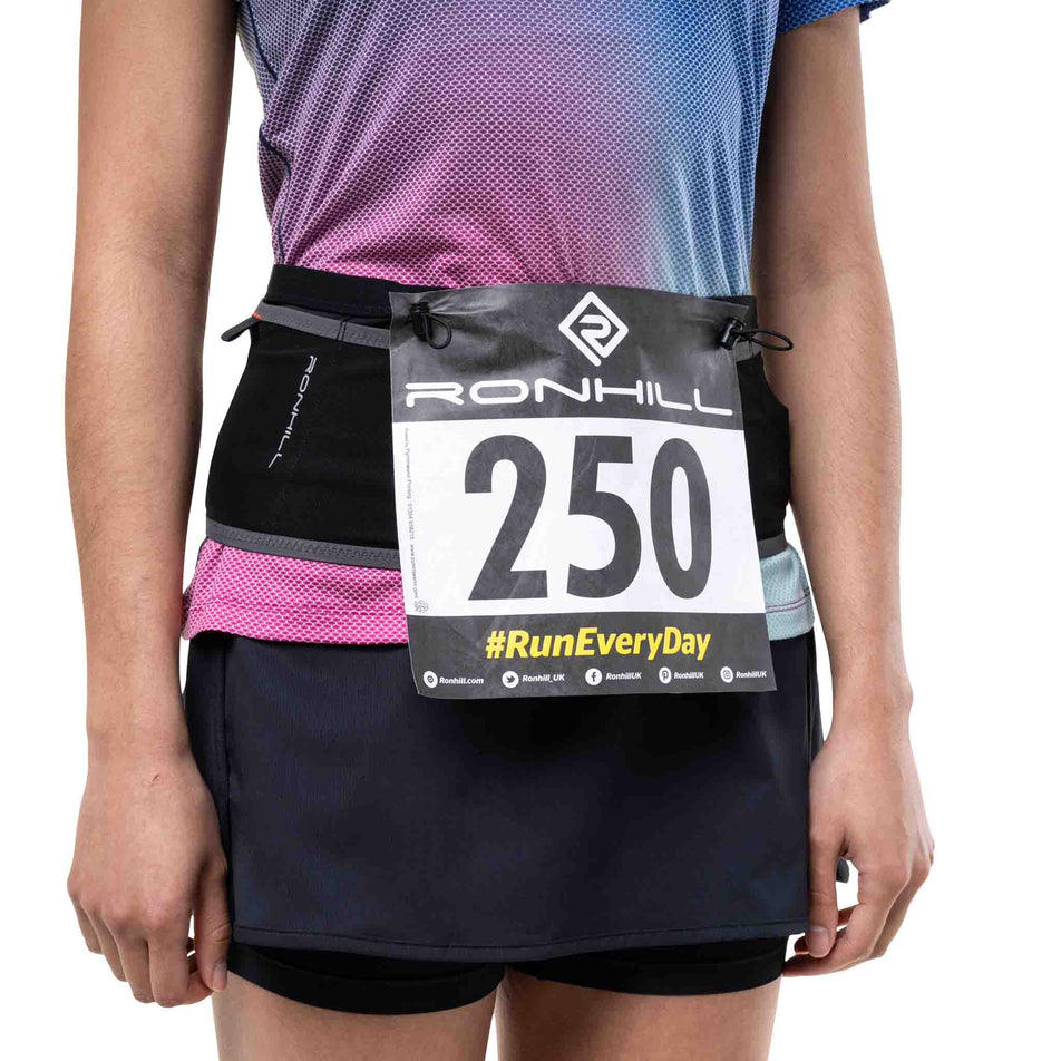 A model demonstrating the race number fasteners on the Ronhill Unisex Speed 360 in the Black/Ronhill Red colourway.