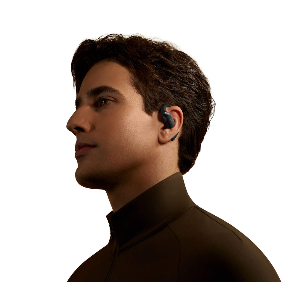 A model wearing an earbud from a pair of Shokz OpenFit 2+ Wireless Earbuds in the black colourway