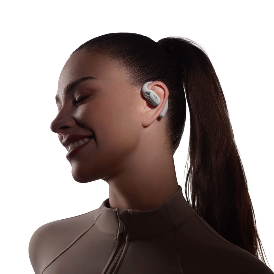 A model wearing an earbud from a pair of Shokz OpenFit 2+ Wireless Earbuds in the grey colourway