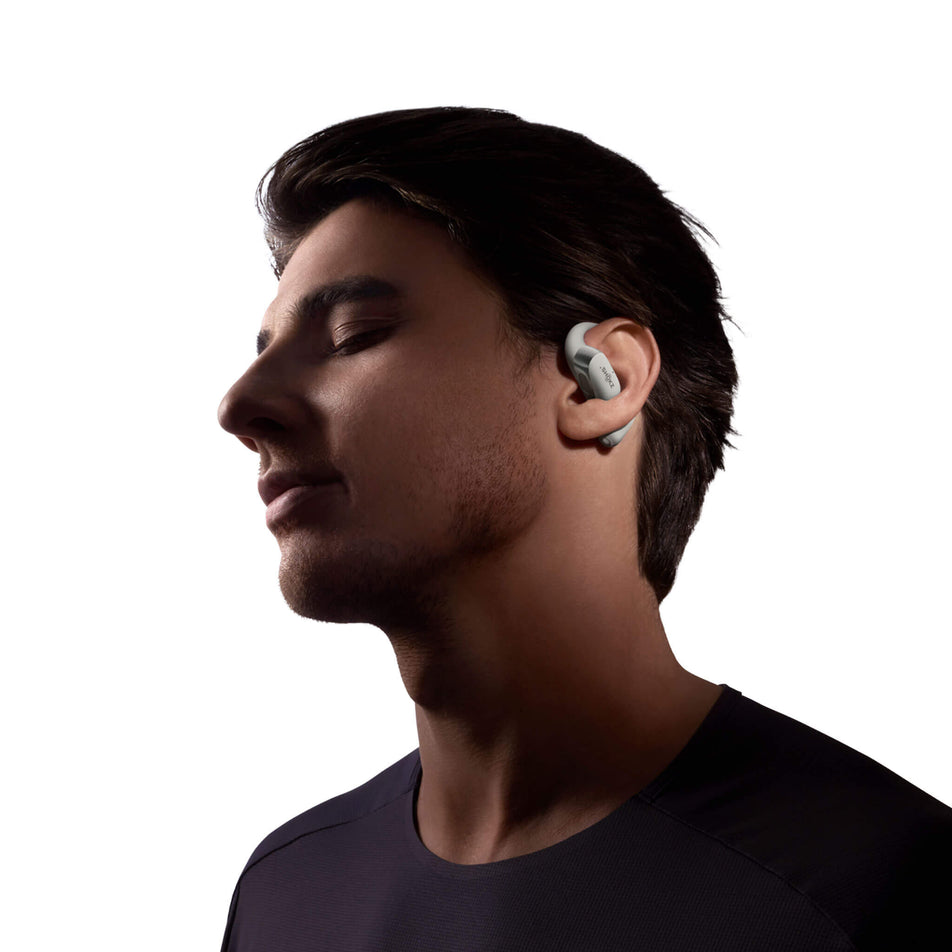 A model wearing an earbud from a pair of Shokz OpenFit 2+ Wireless Earbuds in the grey colourway