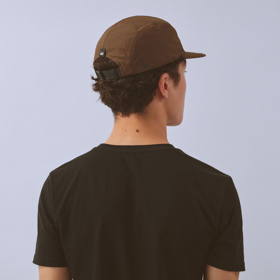 Back view of a model wearing the VAGA Unisex Waterproof Fell Cap in the Brown colourway.