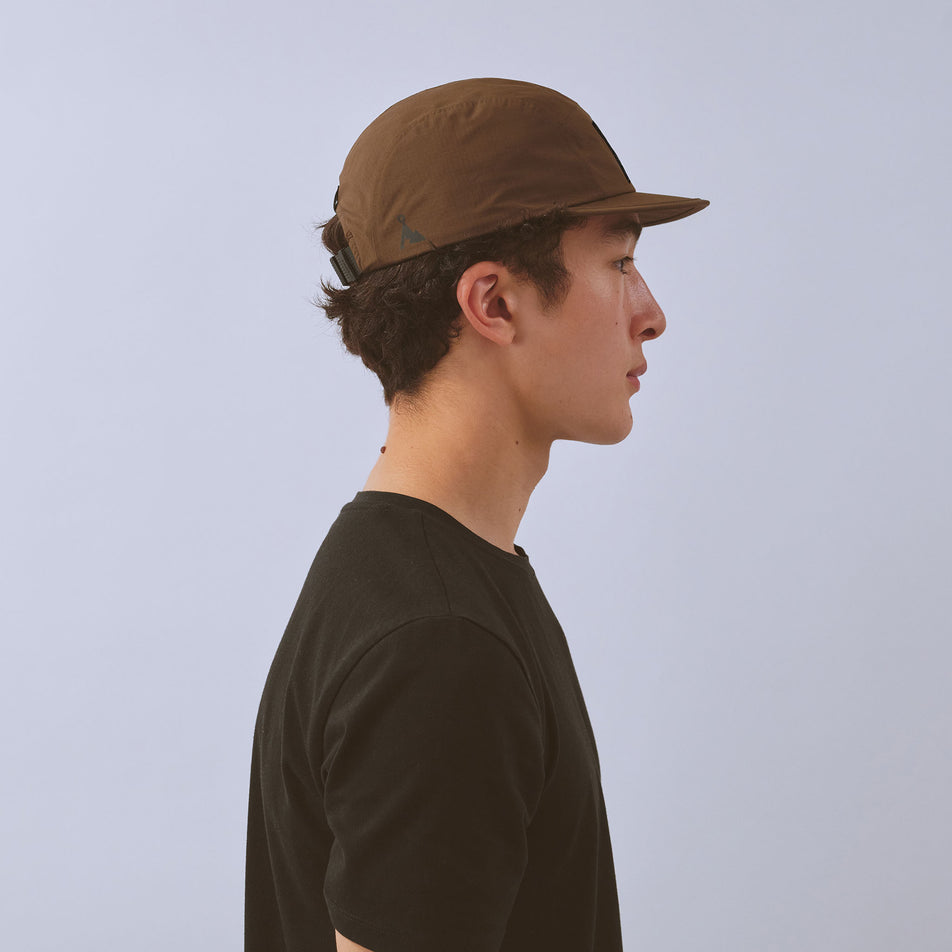 Side view of a model wearing the VAGA Unisex Waterproof Fell Cap in the Brown colourway.