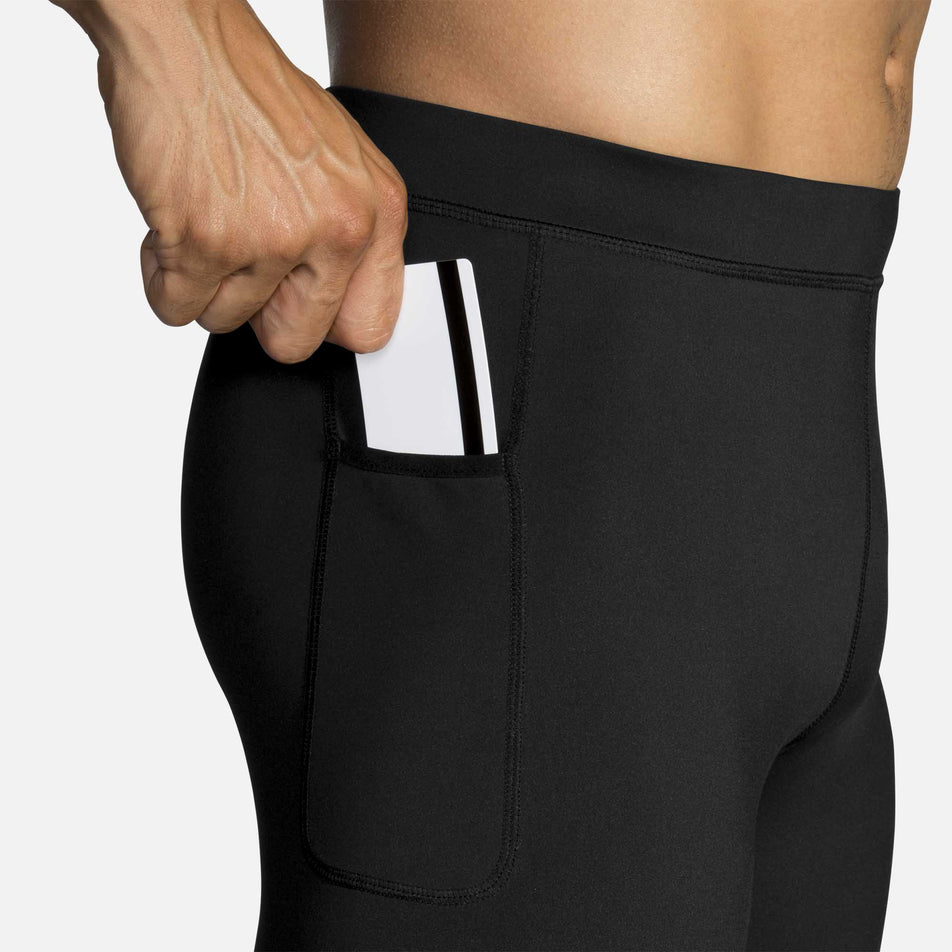 A model wearing the men's Brooks Source Tight and putting a bank card into the right side hip pocket (6935063986338)