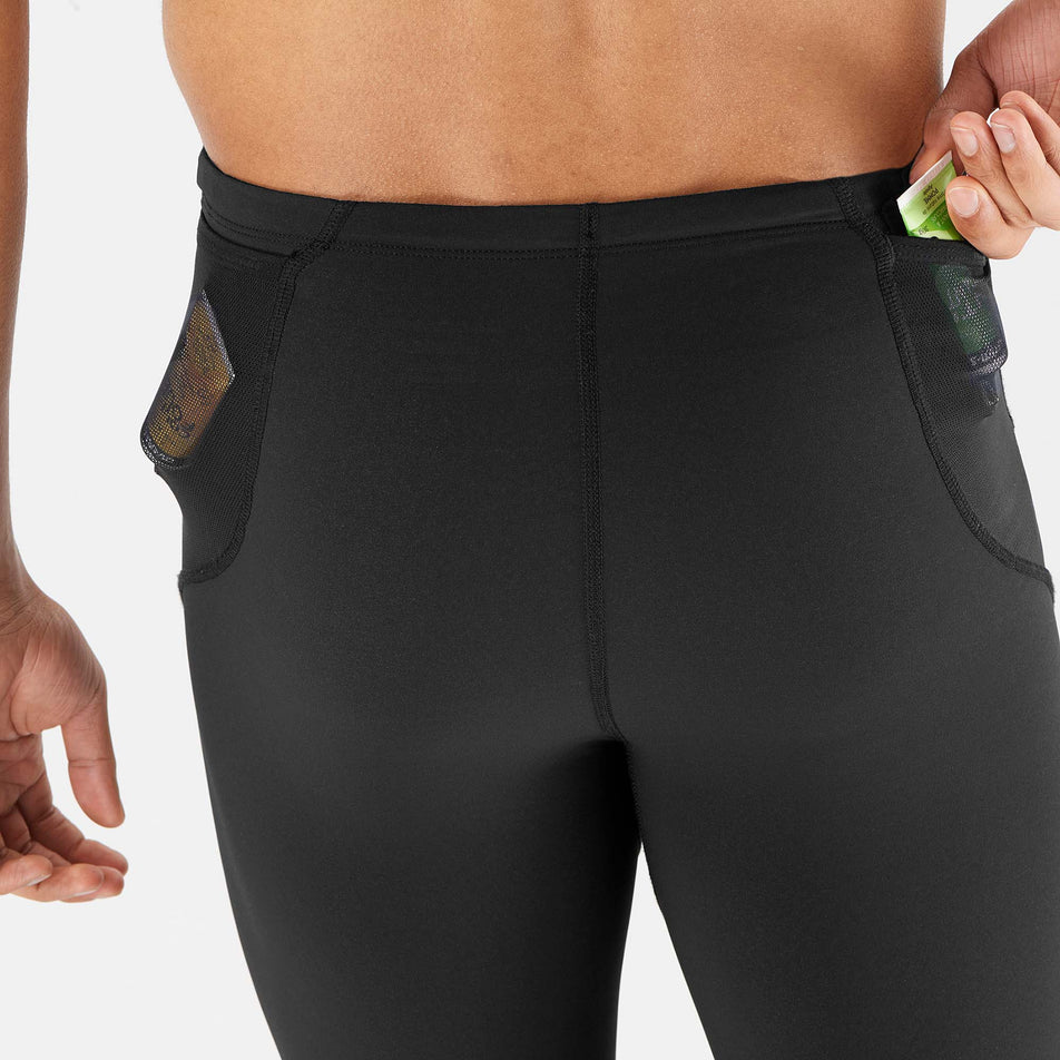 Close-up back view of a model wearing a pair of Salomon Men's Sense Aero Tights in the Deep Black colourway, demonstrating that nutrition can be stored in the mesh pockets on either side of the waistband. (7565961625762)