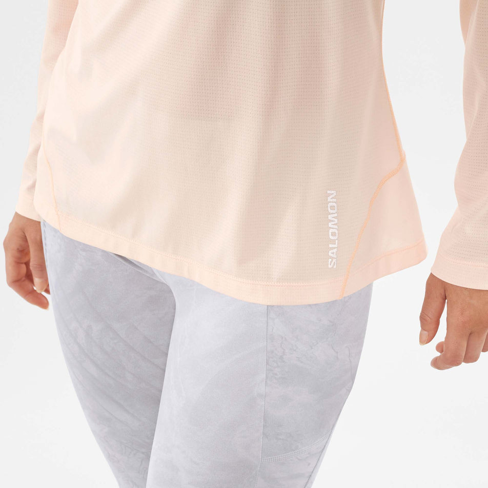 Close-up view of the Salomon logo on the lower front left of a Salomon Women's Cross Run Long Sleeve T-Shirt in the Cream Tan/Heather colourway, being worn by a model (7891226296482)