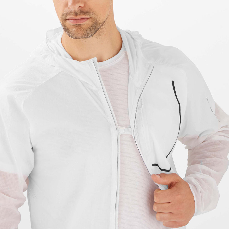 A male mode demonstrating that the Salomon Unisex Bonatti Aero Wind Jacket can be partially fastened closed at the chest, while it is unzipped. (7889368514722)