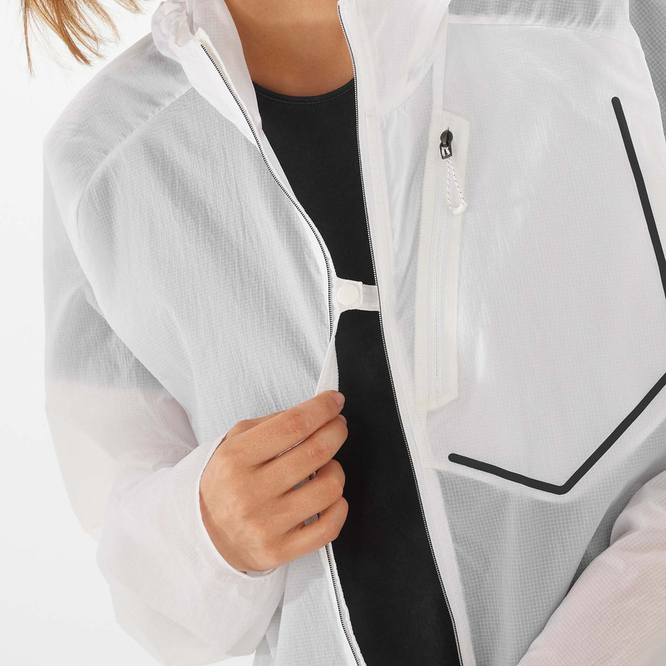 A female mode demonstrating that the Salomon Unisex Bonatti Aero Wind Jacket can be partially fastened closed at the chest, while it is unzipped.  (7889368514722)