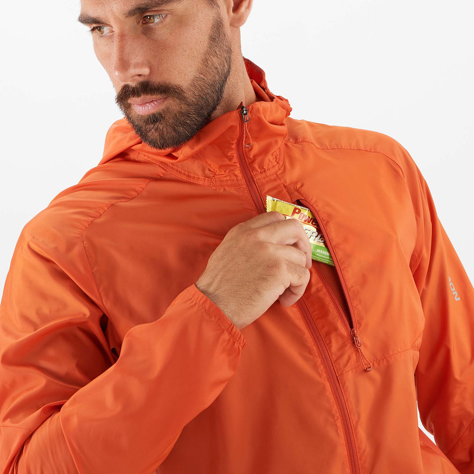 A model taking an energy gel out of the zipped chest pocket on a Salomon Men's Bonatti Cross Wind Jacket Hoodie (7889270866082)