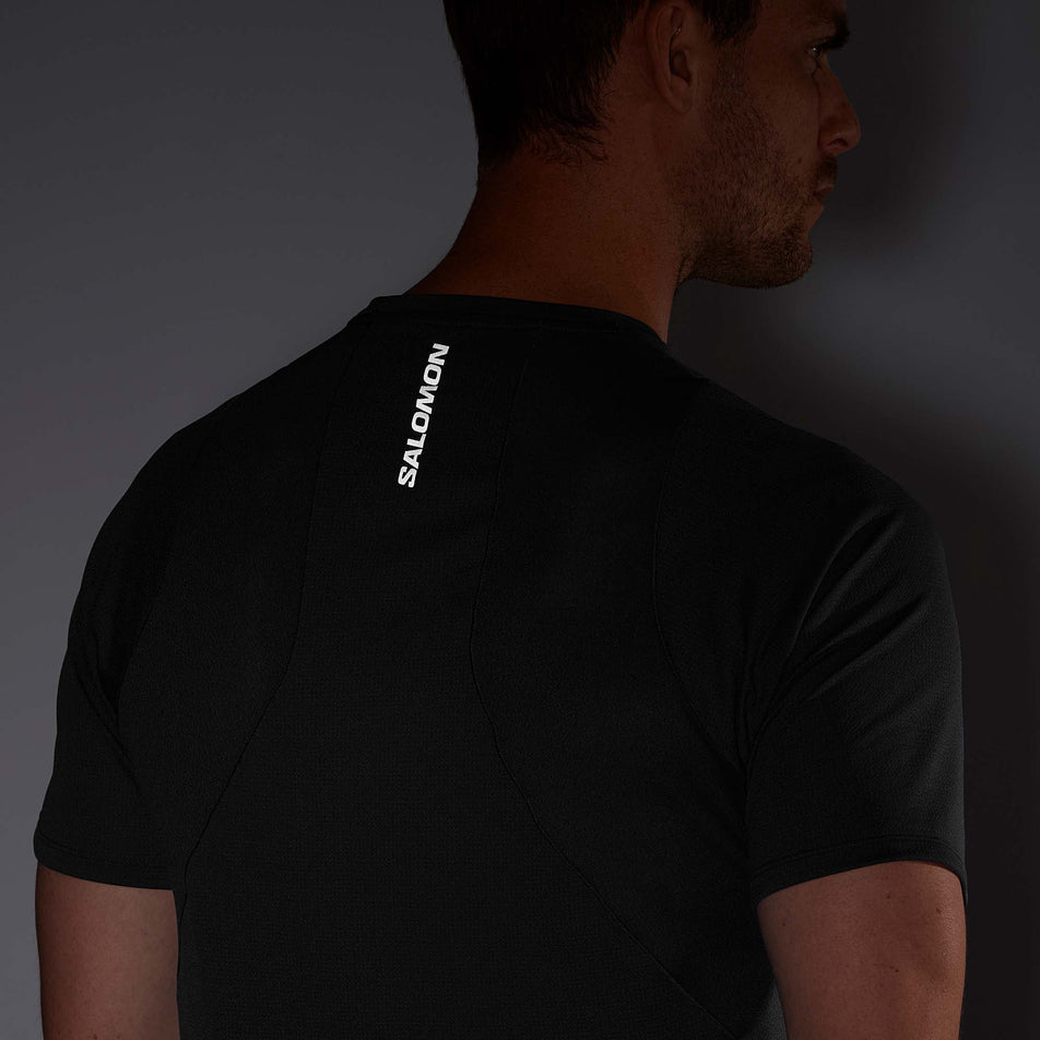 Close-up view of the reflective Salomon logo on the upper back section of a Salomon Men's Sense Aero Short Sleeve T-Shirt in the Deep Black colourway - being worn by a model (7890837635234)