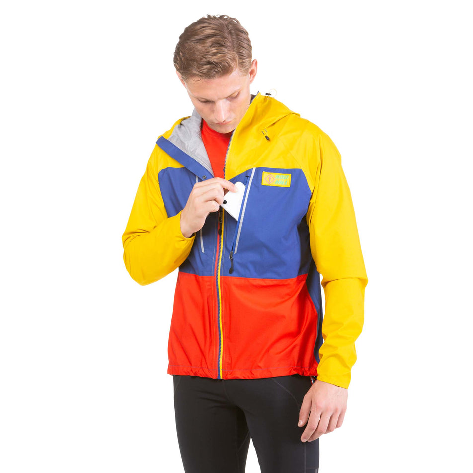 Front view of a model wearing and taking a phone out of the chest pocket on a Ronhill Men's Tech Fortify Jacket in the Dark Cobalt/Solar colourway (7743532925090)
