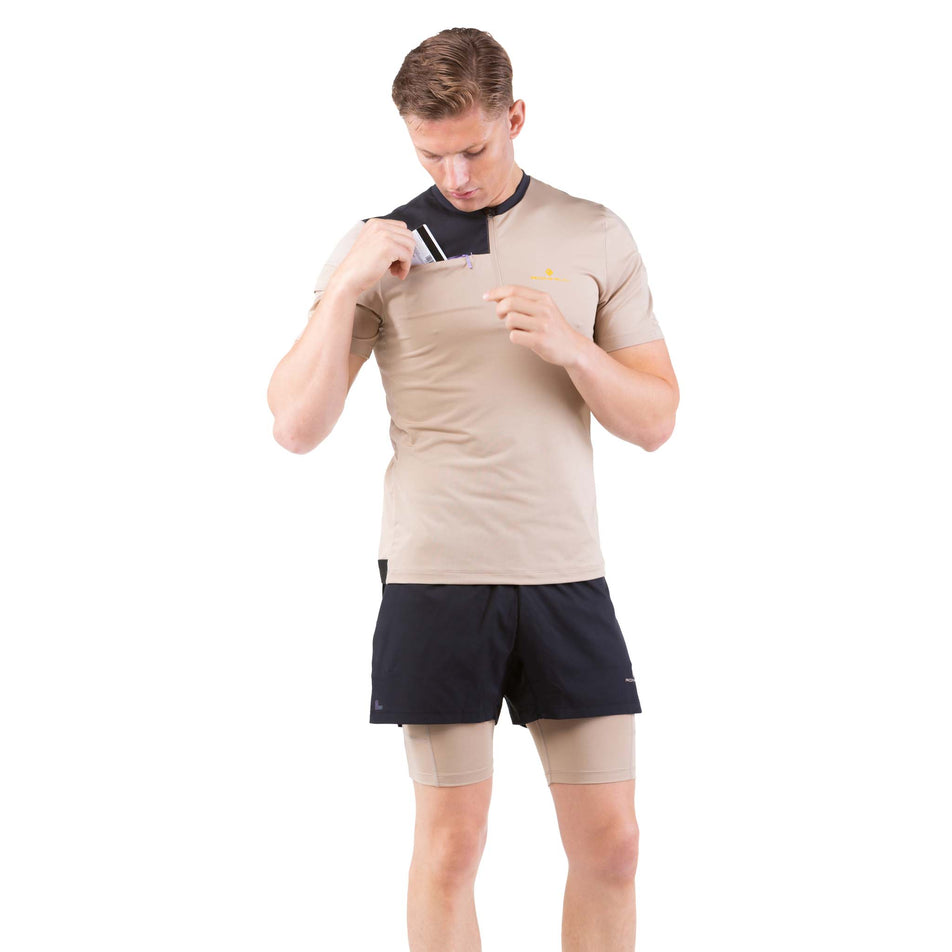Front view of a model wearing a Ronhill Men's Tech Ultra 1/2 Zip Tee in the Latte/Black colourway, and taking a card out of the chest pocket (7744538149026)