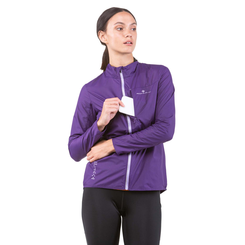 Front view of a model wearing a Ronhill Women's Tech LTW Jacket - fully zipped and taking phone out of chest pocket (7844276043938)