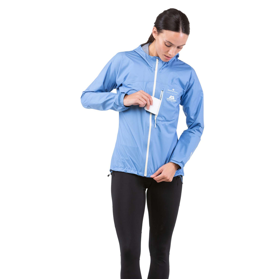 Front view of a model taking a phone out of the chest pocket on a Ronhill Women's Tech Mercurial Jacket (7742604837026)