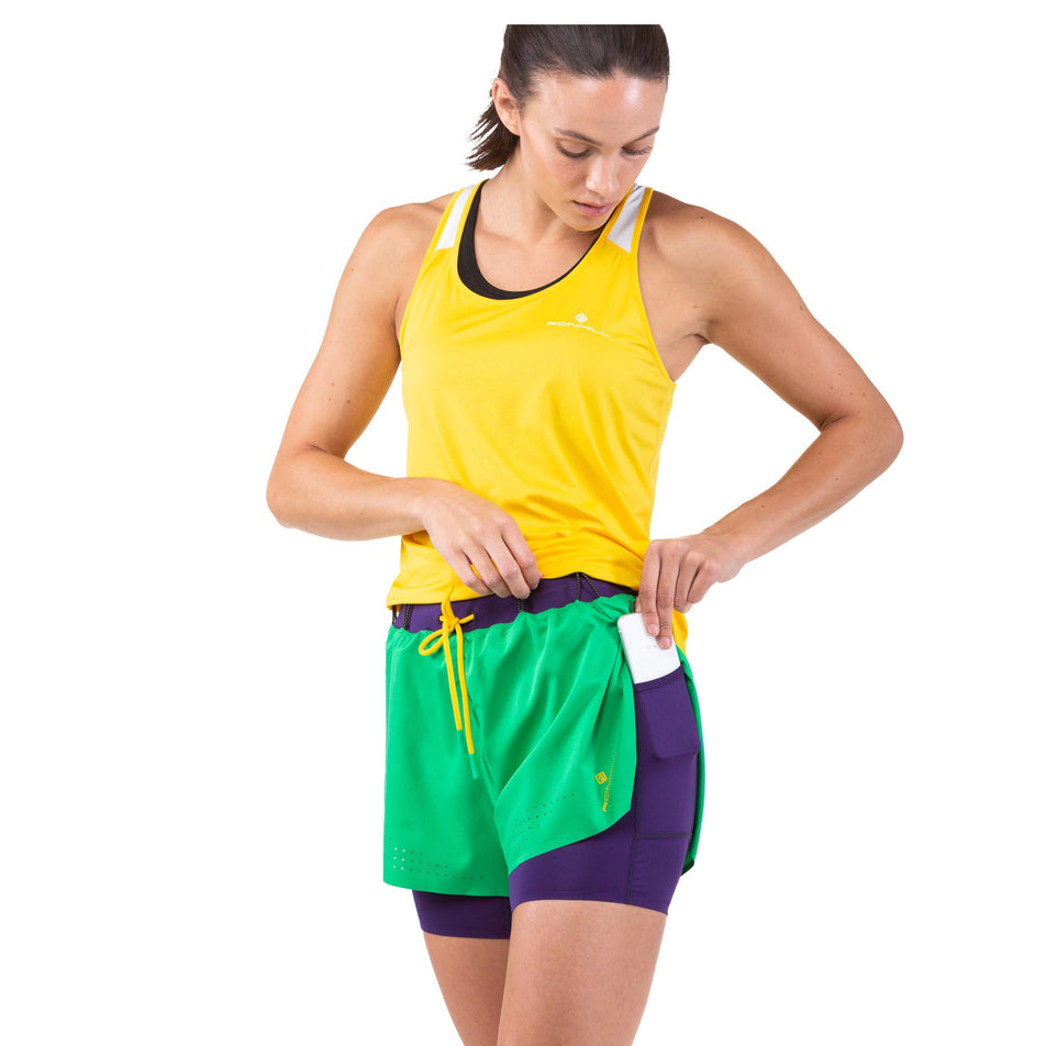 Front view of a model taking a phone out of the side pocket on a pair of Ronhill Women's Tech Distance Twin Shorts (7744909050018)