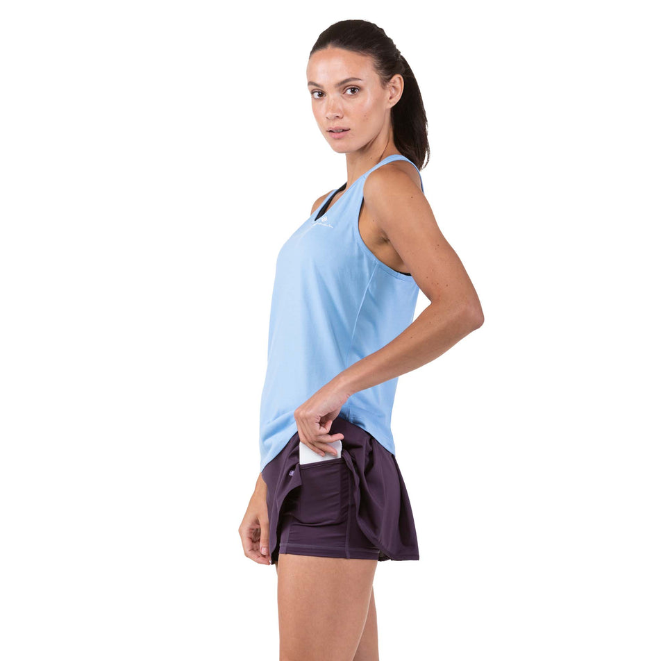 Side view of a model taking a phone out of the side leg pocket on a Ronhill Women's Tech Skort (7744911474850)